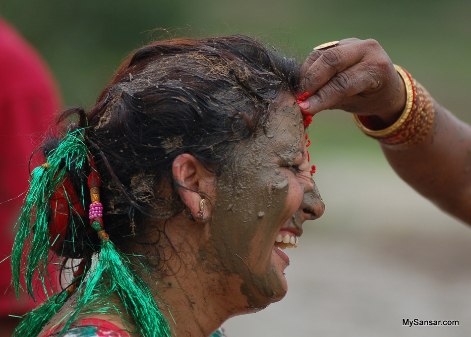 A woman in her smiley and mud her face during Aasar-15 festival, popularly known as Paddy Day (Dhan Diwash) Photo:  Bikash Dware