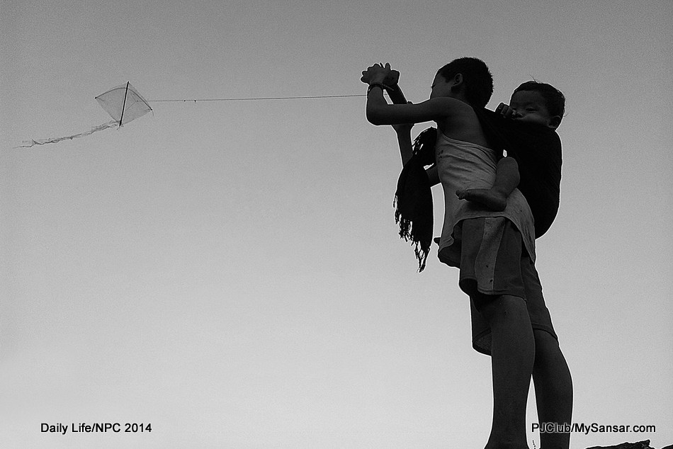 A boy carries his sib on his back as he flies a kite. Photo: Manjil Joshi 